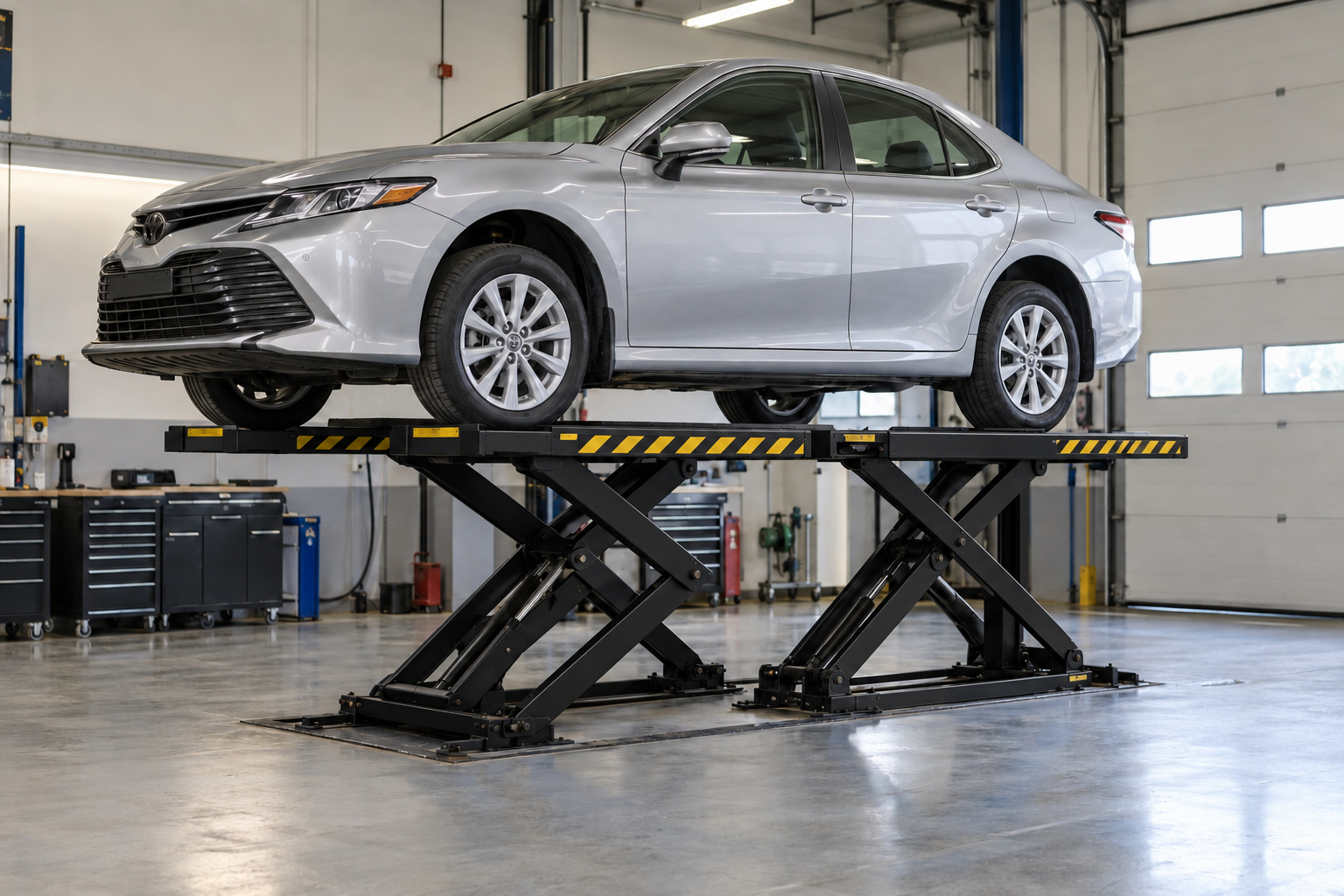 A silver sedan raised on a black scissor car lift in a service bay