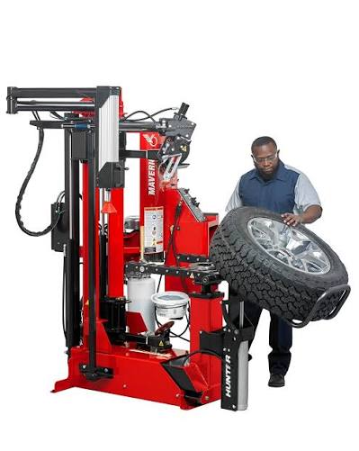 A technician at a red and black tire changer with a wheel on the machine